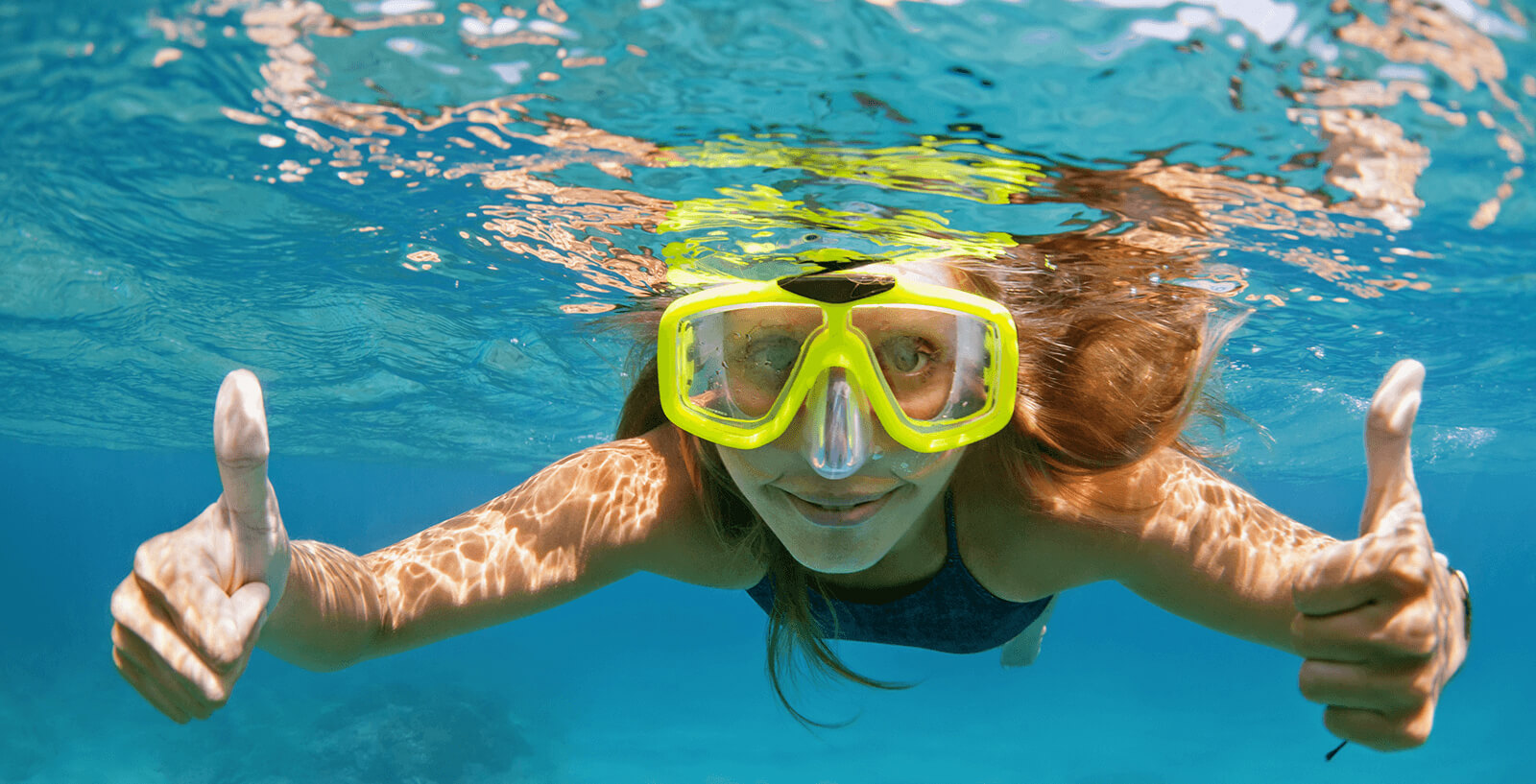 Young woman snorkeling underwater with yellow mask.